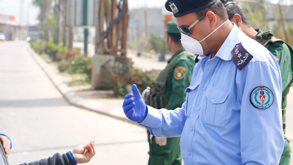 A Palestinian man in a face mask speaks to a person in a car