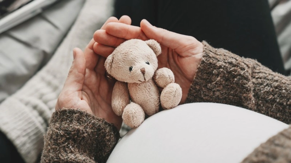A pregnant woman holds a small teddy next to her belly